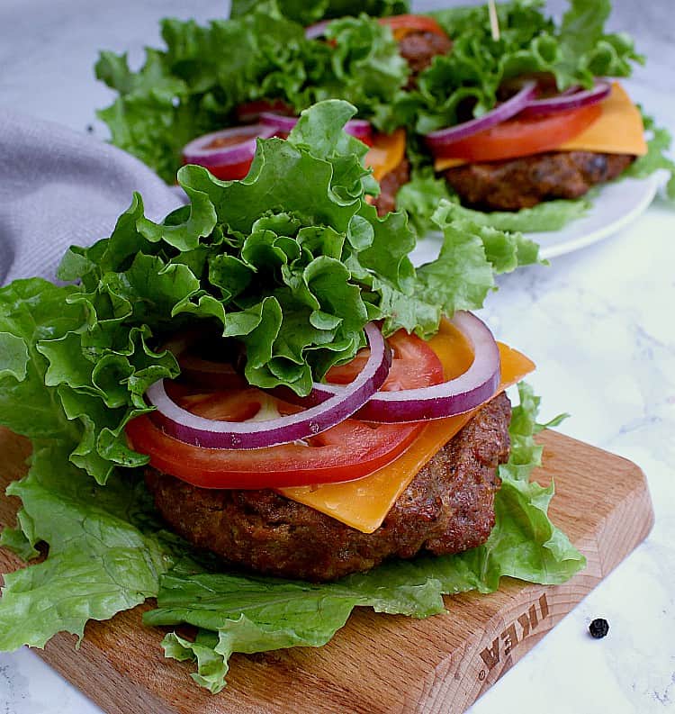 Four Keto Burgers wrapped in leaf lettuce along with cheese, tomato and red onion.