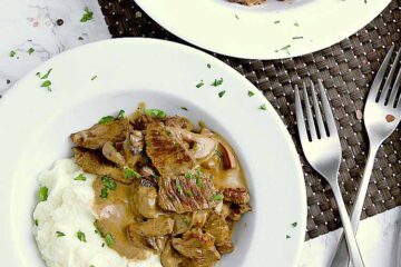 Two white bowls with cauliflower mash, keto beef stroganoff and garnished with fresh parsley.