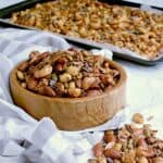 Wooden bowl of keto trail mix infront of a baking sheet filled with the mix.
