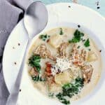 White soup bowl filled with keto zuppa toscana and garnished with grated parmesan cheese. There is a spoon on the bowl.