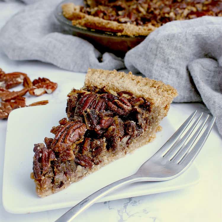 One slice of Keto Pecan Pie on a white plate with a fork, with the full pie behind.