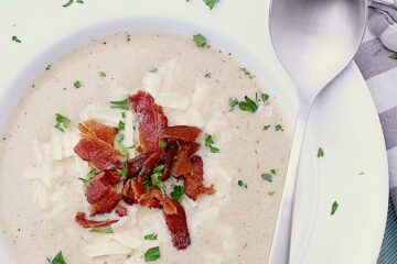 White bowl with Keto Cauliflower Soup that has been garnished with bacon, cheese and parsley.