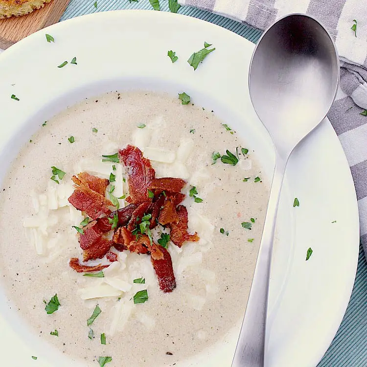 White bowl with Keto Cauliflower Soup that has been garnished with bacon, cheese and parsley.