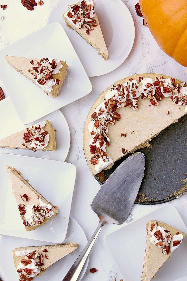 Half a Keto Pumpkin Cheesecake on the pan with the remaining half cut into slices and placed onto plates around the cake.