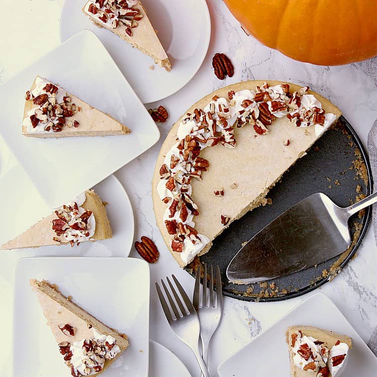 Half a Keto Pumpkin Cheesecake on the pan with the remaining half cut into slices and placed onto plates around the cake.