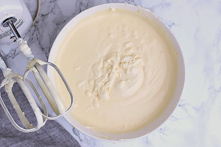 A bowl with the whipped cream cheese and sweetener next to a hand mixer.