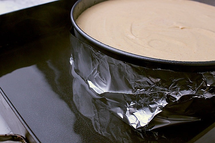 A springform inside a roasting pan, filled with the Keto Pumpkin Cheesecake batter. There is 1/2 an inch of boiling water inside the pan.