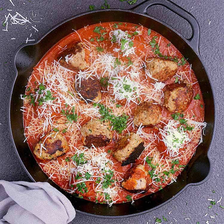 A cast iron skillet with Keto Turkey Meatballs drenched in Keto Marinara Sauce and topped with grated parmesan and parsley.