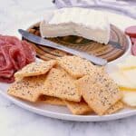 Appetizer plate with brie, cheddar, sausage, salami and a handful of Keto Crackers.