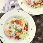 A white dish with zucchini noodles, marinara and chicken, topped with fresh parmesan and parsley.