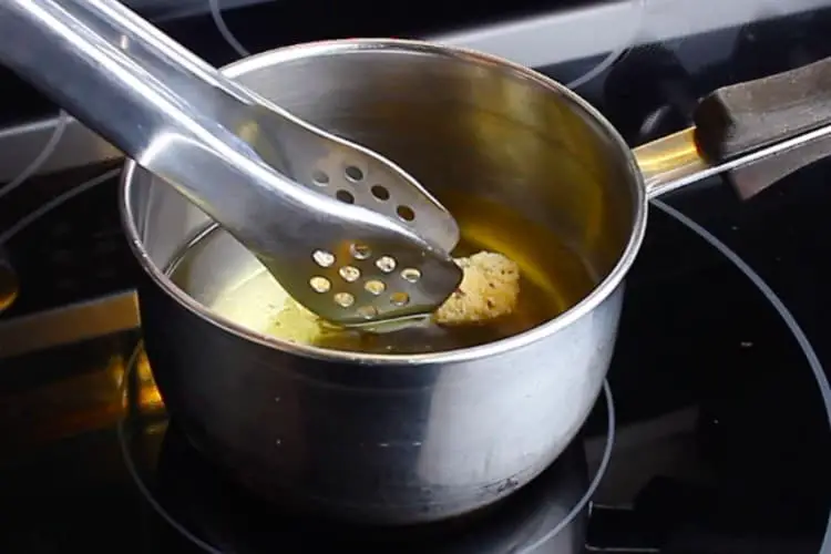 Tongs dropping a Keto Mozzarella Stick inside a small saucepan with oil. 