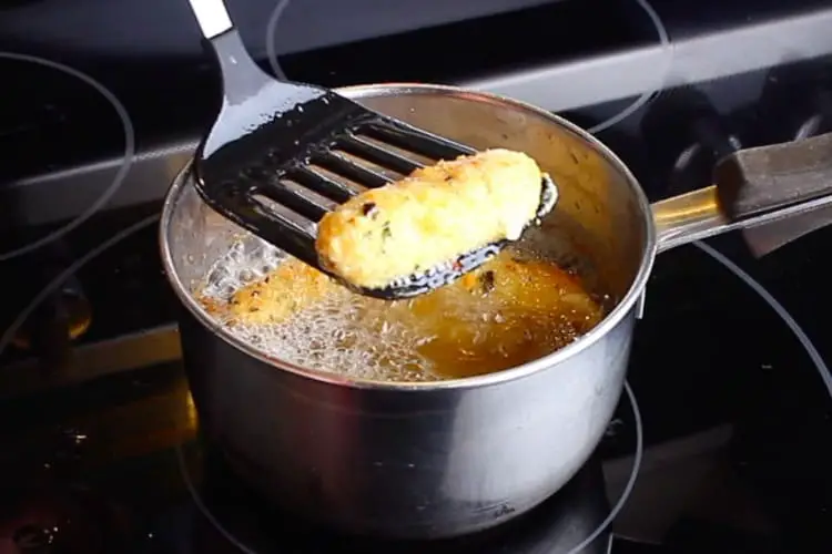 A slotted spatula carefully removing a fried Keto Mozza Stick from the hot oil.