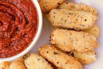 Plate of stacked Keto Mozzarella Sticks beside a bowl of pizza sauce.