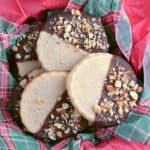 Tin with Christmas paper and Keto Shortbread Cookies that have been dipped in chocolate and sprinkled with chopped almonds and sea salt.