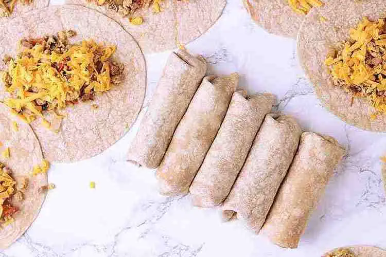 5 wrapped Keto Breakfast Burritos in a line next to some unwrapped burritos.