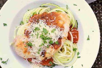 A bowl with Keto Chicken Parmesan, garnished with parmesan and parsley.