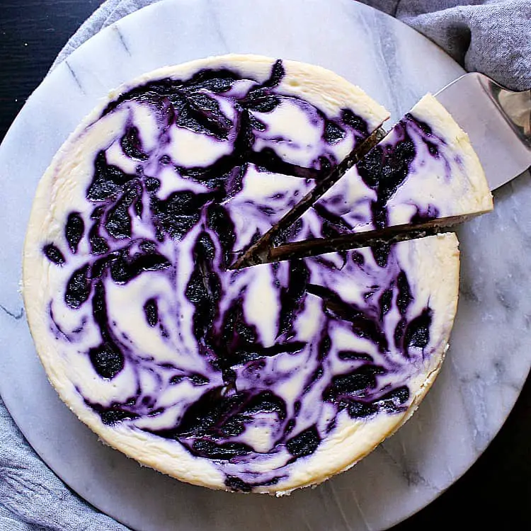 A Keto Blueberry Swirl Cheesecake with one slice being removed.
