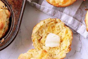 A pile of Keto Cheddar Biscuits, one sliced in half with butter.