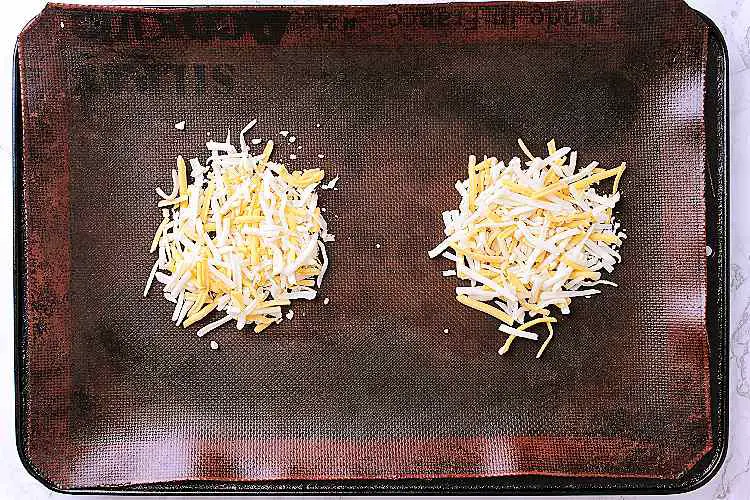 Baking sheet with 2 clumps of shredded cheese.