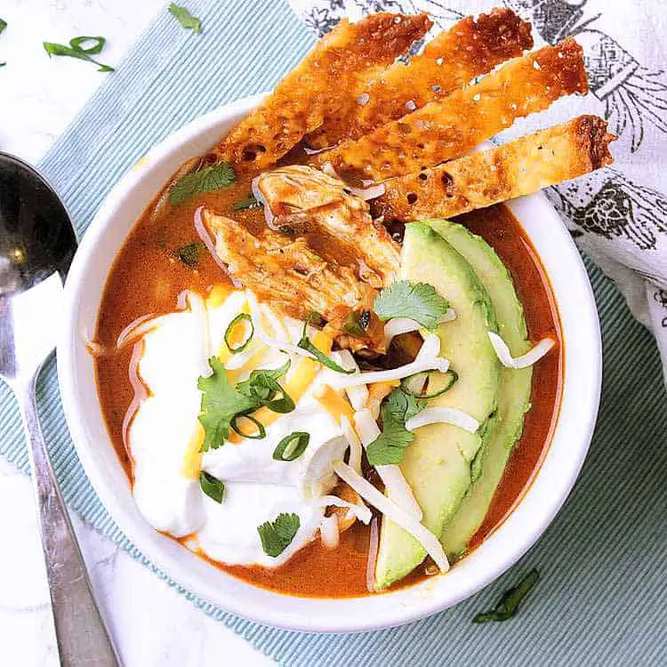 A bowl of Keto Chicken Tortilla Soup, garnished with avocado, sour cream, green onion, cilantro and cheese strips.