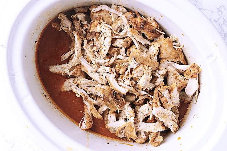 Slow cooker with shredded chicken on top of sauce.