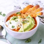 A white bowl with keto chicken tortilla soup and topped with sour cream, avocado and cheese strips.