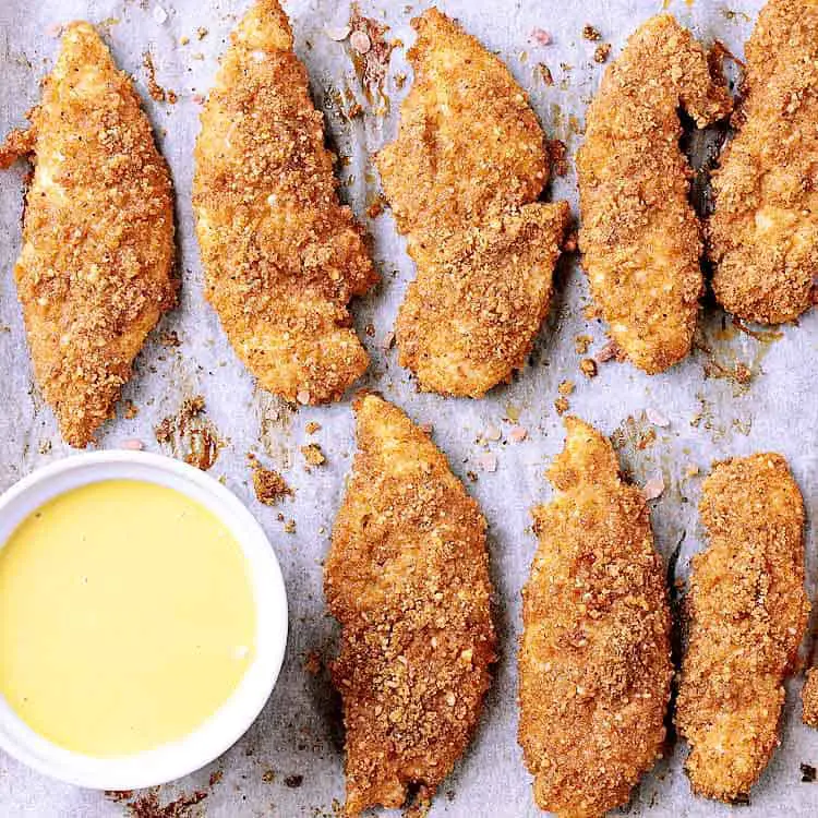 A baking sheet with crispy keto chicken tenders next to a bowl of keto honey mustard.